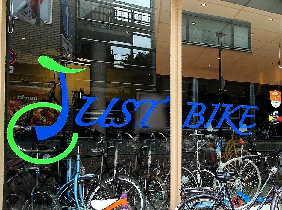De etalage van Just Bike met het logo op de ruit en fietsen in de winkel