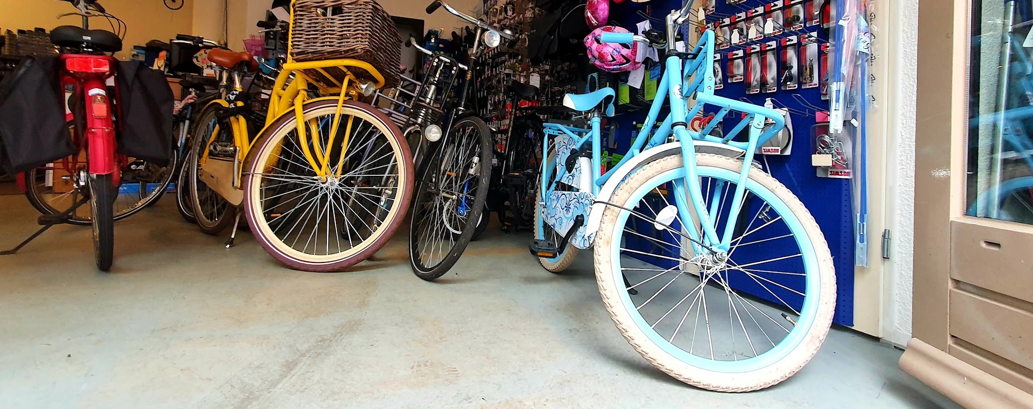 Binnen bij Just Bike: fietsen op een rij voor de wand met onderdelen en accessoires